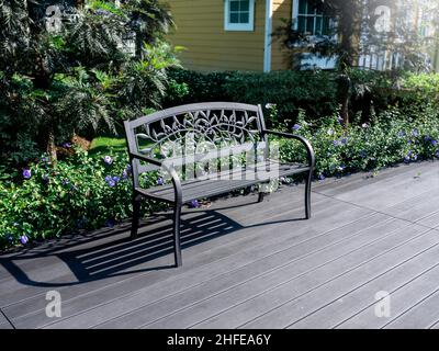 Empty black wrought iron bench decorated on the dark wood plank floors near the garden in front of the building. Stock Photo