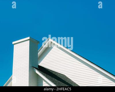 A white chimney bricks on the roof of the big wooden white house against blue sky background on a sunny day with copy space. Stock Photo