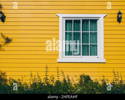 A white house window with glass, green curtain decoration with wall lamps on the yellow wooden resident, view from outdoor. Stock Photo