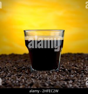 Espresso om glass on coffee beans on yellow background Stock Photo