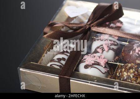 Candies in chocolate glaze. In a gift box. Tied with a ribbon tied into a bow. On a black background. Stock Photo
