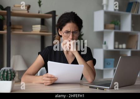 Worried unhappy young woman reading paper letter with bad news. Stock Photo