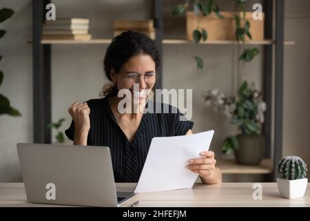 Hispanic woman celebrating document success in modern office with ...