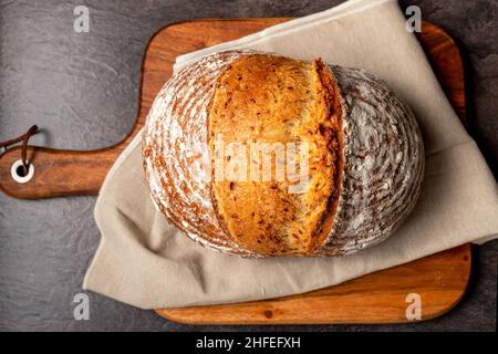 Wholemeal sourdough bread on brown chopping board. Warm mood, concept of healthy homemade food. Stock Photo