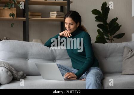 Pleasant happy young hispanic woman using laptop at home. Stock Photo