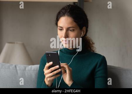 Interested young woman in wired earphones using cellphone. Stock Photo