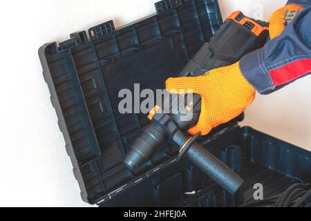 Hands in protective gloves hold  a rotary hammer. worker, professional with hammer drill perforator. Stock Photo
