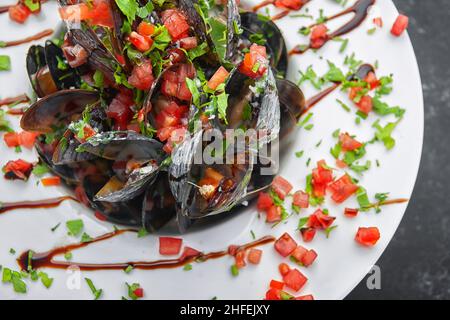 Boiled Mussels with vegetables, herbs and sauce, on a white plate Stock Photo