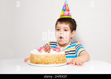 A child in a festive cap blows out the candles on the cake on his birthday Stock Photo