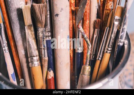 A bunch of well used painter's brushes with wooden handle in a metal bucket. Creative background Stock Photo