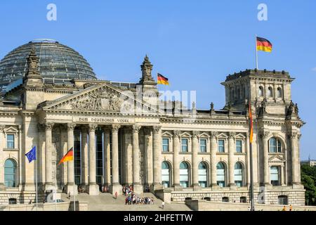 View of front exterior of Reichstag building with glass dome on rooftop in summer. Crowd of people queue at entrance. Clear blue sky background. Stock Photo