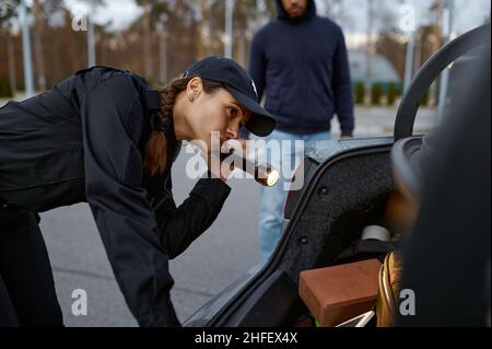 Woman police officer inspecting car with flashlight Stock Photo