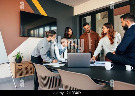 Diverse businesspeople discussing some reports in a boardroom. Group of multicultural businesspeople standing around a table in a modern office. Young Stock Photo