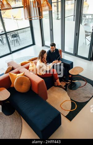 High angle view of two businesspeople working in an office lobby. Two modern businesspeople using a digital tablet while having a discussion. Two youn Stock Photo