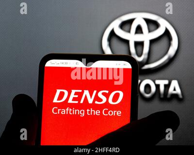 In this photo illustration, the Denso Corporation logo is seen displayed on a smartphone screen with the Toyota logo in the background. Stock Photo