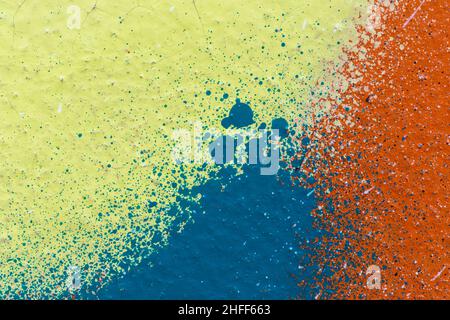 Macro close-up of bright yellow, blue and orange spray paint with colorful splashes. Abstract full frame textured splattered graffiti background. Stock Photo