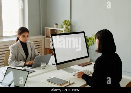 Two Asian businesswomen using computers with white screen while working at desk in office Stock Photo