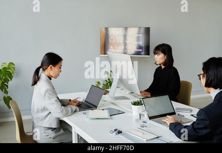 Minimal shot of group of Asian business people working with computers in modern white office Stock Photo