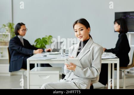Minimal portrait of elegant Asian businesswoman looking at camera while taking notes in meeting Stock Photo