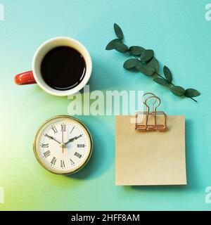 Notepad, clock, cup of coffee, green leaf on mint green background. office desk, workspace. top view Stock Photo