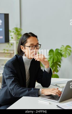 Vertical portrait of young Asian businessman using laptop while working in modern office Stock Photo
