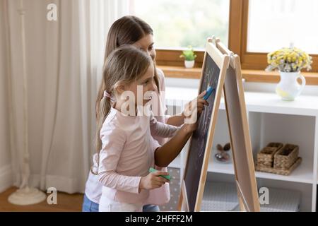 Mother and little daughter holding chalks drawing on board Stock Photo