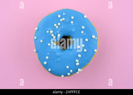 Bright donut on a pink background with space for text. Donut with blue icing and beads top view. Sweet round donut with a hole. Stock Photo