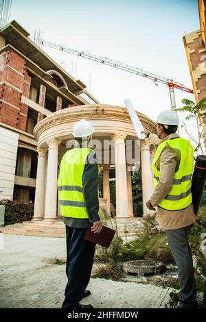 Two construction workers are looking at the construction area while explaining the plans Stock Photo