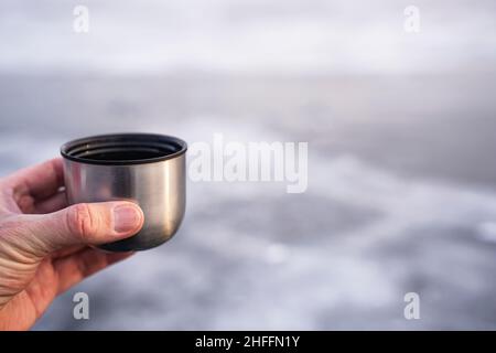 Morning coffee on Lake Baikal in winter, The image is a close-up of a man's hand holding a thermos cup Stock Photo