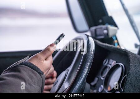 Driver hand holding Smartphone for using GPS navigation while the hovercraft is moving on frozen Lake Baikal, to read data in a web browser or text me Stock Photo