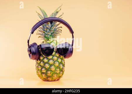 Creative idea of a pineapple image of a person headphones and glasses as a relaxing tourist on vacation. On a yellow background. Stock Photo