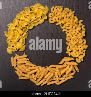 variety of uncooked pasta arranged in circle, isolated on black slate background, diet and food concept, top down view with copy space Stock Photo
