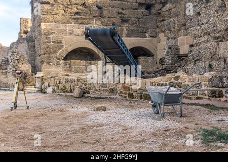 archaeological site among antique ruins with a conveyor for ground, theodolite and wheelbarrow in the foreground Stock Photo