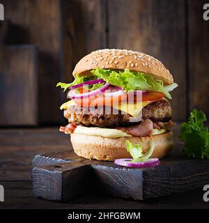 Hamburger with bacon, turkey burger meat, cheese, tomato and lettuce on wooden background. Tasty burger. Close up Stock Photo