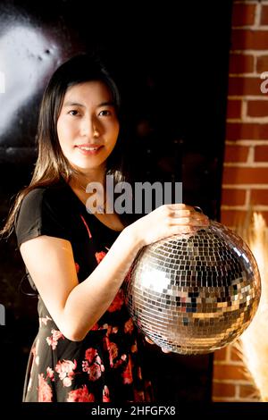 Young East Asian Woman in Floral Print Dress Holding a Mirror Ball Stock Photo