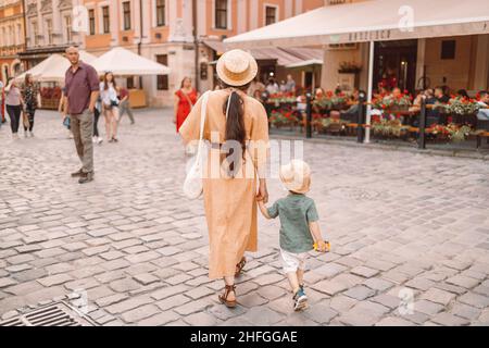 Back view of a mother with a child by the hand walking around the old city of lviv on a summer sunny day. City center with crowd of people Stock Photo