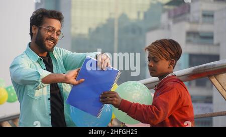young man help poor boy and give notebook in hand Stock Photo