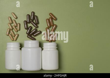 Multi-colored capsules with dietary supplements fly out of three white plastic jars on a green background Stock Photo