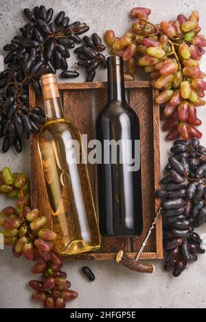 Two Wine bottles with grapes and wineglasses on old gray concrete table background with copy space. Red wine with a vine branch. Wine composition on r Stock Photo