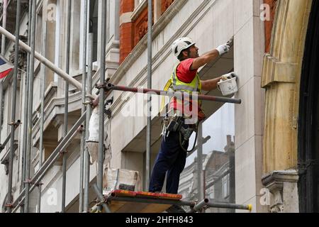 London, England - June 2020: Painter and decorator standing on a scaffolding poles and wooden platform filling in cracks on the outside of a building Stock Photo