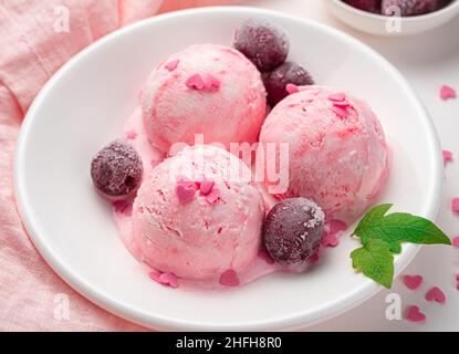Three balls of ice cream with frozen cherries and hearts in a white plate. Side view, close-up. Stock Photo