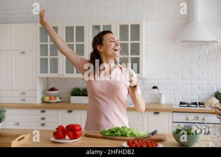 Happy young woman having fun, cooking in modern kitchen. Stock Photo