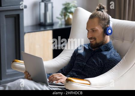 Happy relaxed young man in headphones using computer. Stock Photo