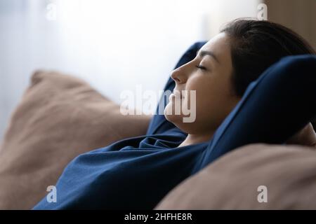 Peaceful happy young Indian woman resting on cozy sofa. Stock Photo