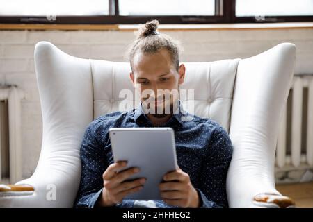 Happy relaxed young man using digital tablet at home. Stock Photo