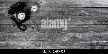 Aged wood office desk table with retro rotary telephone, pen, clock and coins. Top view with plenty of copy space. Stock Photo