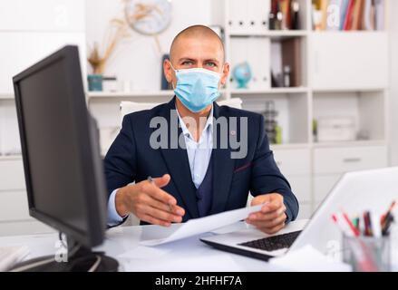 Office worker in a protective mask works behind laptop Stock Photo