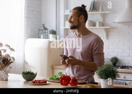 Happy young man using cellphone, preparing food. Stock Photo
