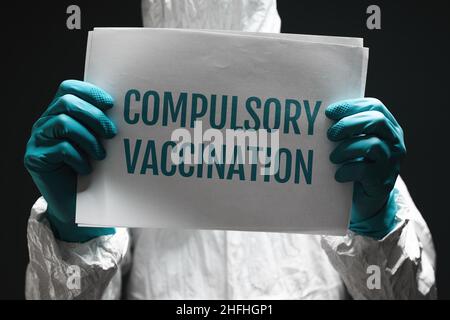 Compulsory vaccination note on poster, medical worker holding paper with text, selective focus Stock Photo