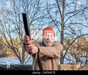 senior man (in late 60s) is exercising with a steel indian club in his backyard, winter afternoon, fitness over 60 concept Stock Photo